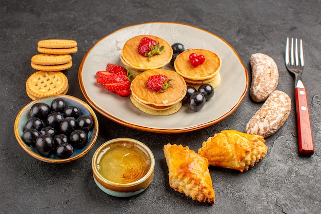 Frente panquecas deliciosas com bolos e frutas em um bolo doce de frutas de superfície escura