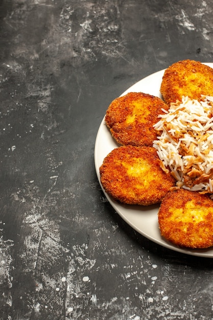 Frente saborosas costeletas fritas com arroz cozido na mesa escura foto refeição prato de carne