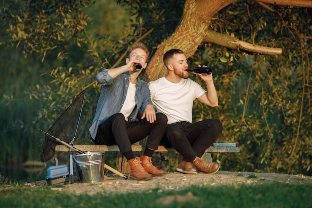 Friends está sentado perto de uma árvore e pescando. dois pescadores conversando e bebendo cerveja