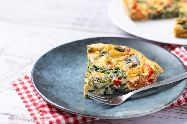 Foto grátis fritada italiana feita com espinafre, tomate, cebola e pimentão na mesa de madeira branca