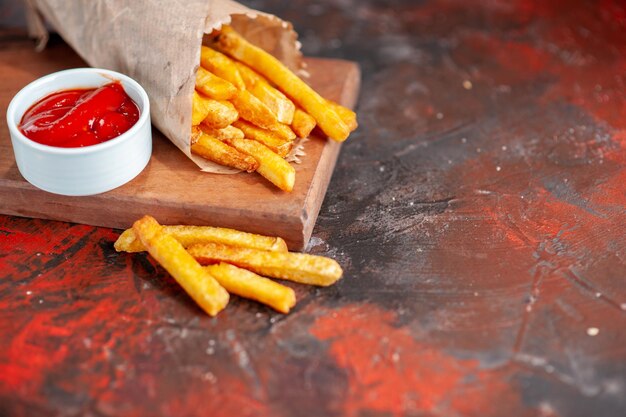 Fritas deliciosas batatas fritas com ketchup na superfície escura da placa de corte