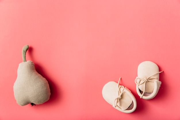 Fruta de pêra recheada e par de sapatos de bebê em fundo colorido