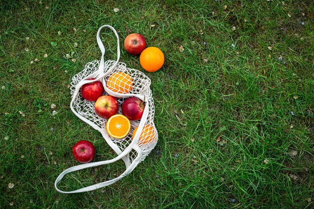 Frutas brilhantes em um saco de corda branca na grama