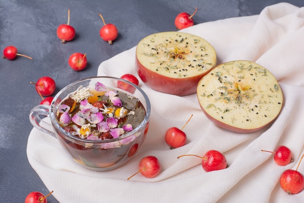 Frutas cortadas pela metade, cerejas e copo de suco com rodela de limão e flores em azul com toalha de mesa