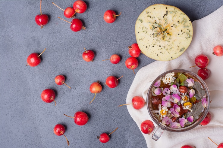 Foto grátis frutas cortadas pela metade, cerejas e copo de suco com rodela de limão e flores em azul com toalha de mesa