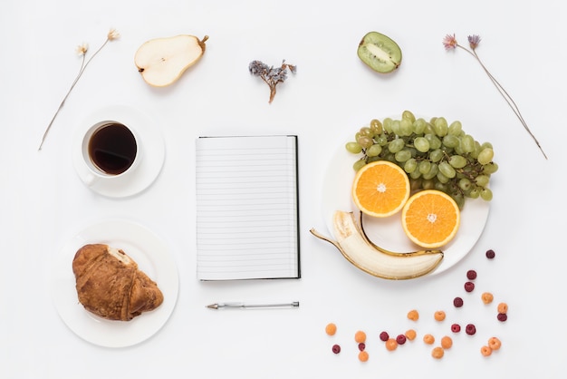 Foto grátis frutas dispostas um rosto humano no prato com croissant; café e flores secas em fundo branco