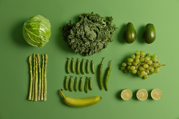 Frutas e vegetais crus verdes saudáveis. Repolho fresco colhido, limão, abacate, aspargos, ervilhas, uva, pimenta e banana isoladas em um fundo vívido. Conjunto de produtos naturais orgânicos.