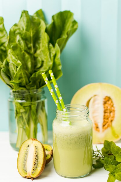 Frutas perto de ervas e copo com coquetel e palhas