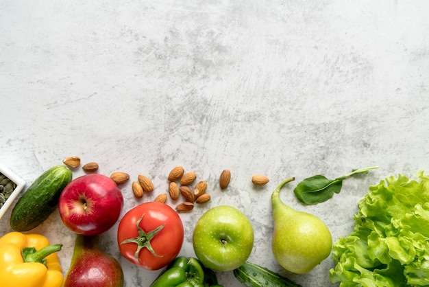 Frutas saudáveis e frescas; legumes e amêndoas sobre superfície texturizada de cimento branco