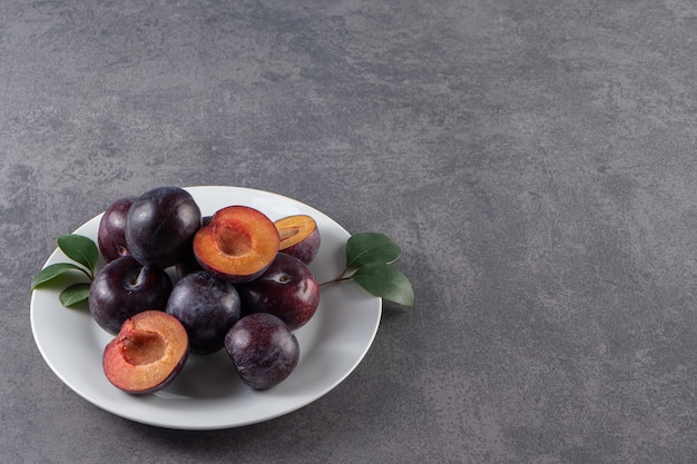 Foto grátis frutas suculentas de ameixa vermelha inteiras e fatiadas colocadas em um prato branco