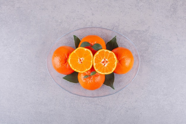 Frutos inteiros de laranja com tangerina fatiada colocados sobre uma superfície de pedra.