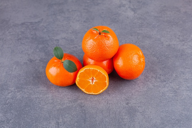 Frutos inteiros e fatiados de tangerina com folhas colocadas sobre uma mesa de pedra.