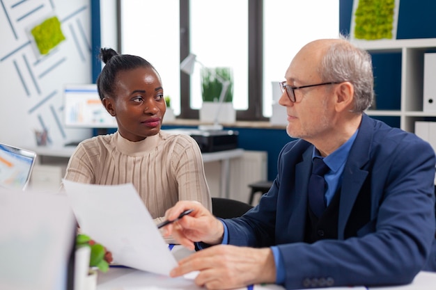 Funcionário africano discutindo com o executivo sênior procurando gráficos financeiros na sala de reuniões da empresa iniciante