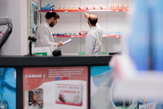 Foto grátis funcionário da farmácia olhando pacotes de medicamentos enquanto trabalhava no estoque de comprimidos na farmácia. os farmacêuticos são treinados em farmacologia e são capazes de preencher e dispensar medicamentos prescritos com precisão.