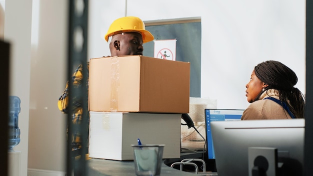 Funcionários afro-americanos que trabalham com carga em caixas, usando embalagens cartonadas do estoque do depósito. Homens e mulheres preparando estoque para distribuição e embarque, controle de qualidade.