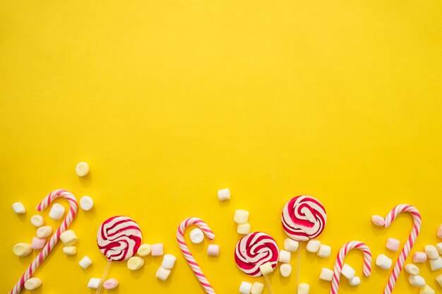 Fundo amarelo com bastões de doces, pirulitos e marshmallows