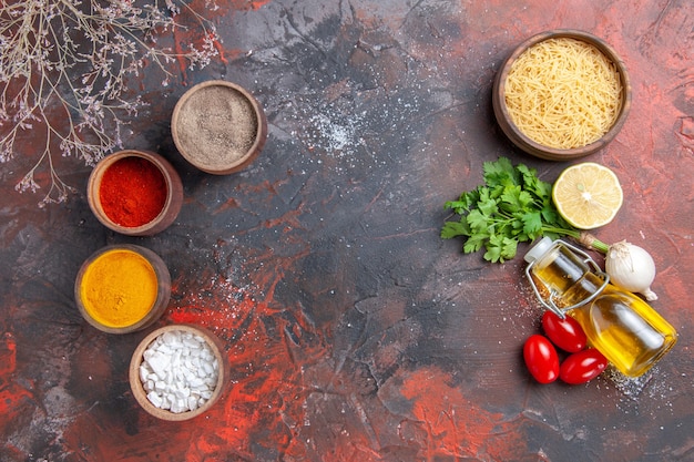 Fundo de jantar massas crus, limão, verde, garrafa de óleo e especiarias diferentes na mesa escura