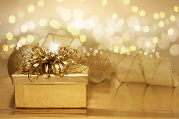 Foto grátis fundo dourado do natal com um presente e bokeh luzes