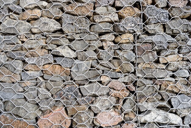 Fundo texturado de Gabion, parede de rocha com cerca de malha de arame.