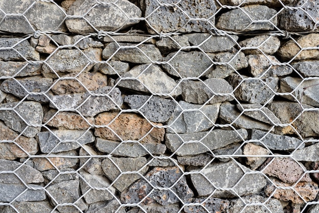 Fundo texturado de Gabion, parede de rocha com cerca de malha de arame.
