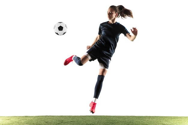 Foto grátis futebol feminino jovem ou jogador de futebol com cabelo comprido em roupas esportivas e botas chutando a bola para o gol no salto isolado no fundo branco. conceito de estilo de vida saudável, esporte profissional, hobby.