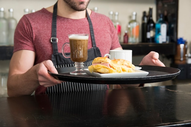 Garçom masculino, segurando o hambúrguer e coquetel na bandeja no bar