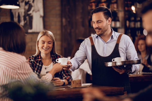 Garçom sorridente servindo café para hóspedes do sexo feminino em um café