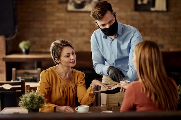 Garçom usando máscara protetora enquanto recomenda algo do menu para seus clientes