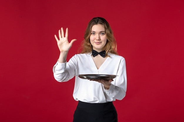 Foto grátis garçonete confiante mulher borboleta no pescoço e segurando a bandeja mostrando cinco em fundo vermelho