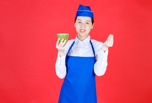 Garçonete de mulher de uniforme em pé e segurando uma tigela verde.