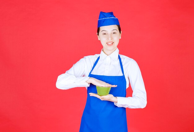 Garçonete de mulher de uniforme em pé e segurando uma tigela verde.