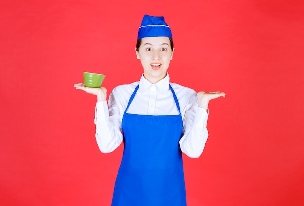 Garçonete de mulher de uniforme em pé e segurando uma tigela verde.