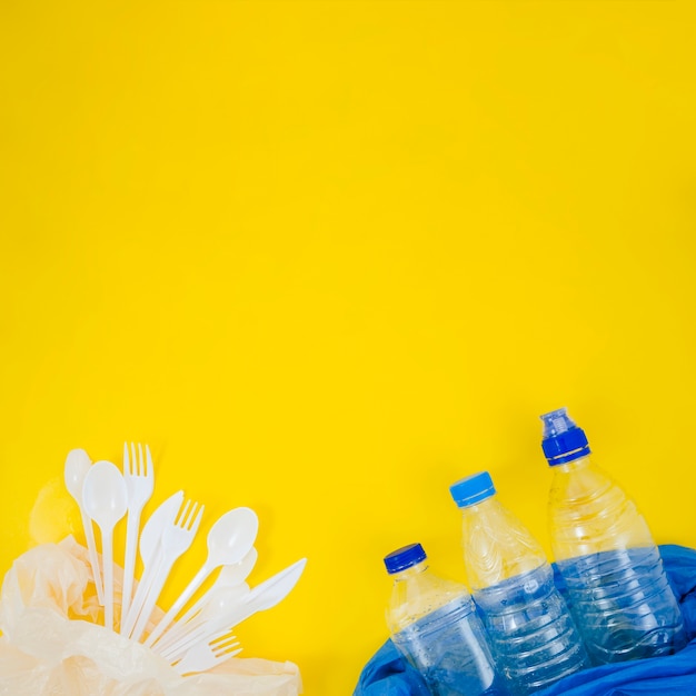 Foto grátis garfo de plástico e colher com garrafa de plástico vazia em saco plástico sobre o pano de fundo amarelo