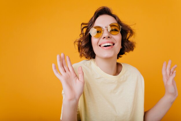 Garota adorável inspirada com cabelo ondulado dançando no espaço laranja