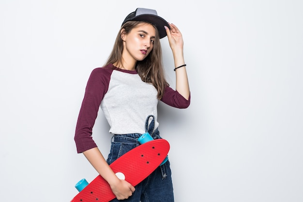 Garota adorável skatista segurando um skate vermelho nas mãos, isolado na parede branca