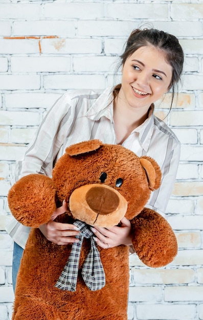 Foto grátis garota adorável sorridente segurando o ursinho de pelúcia e olhando de lado foto de alta qualidade