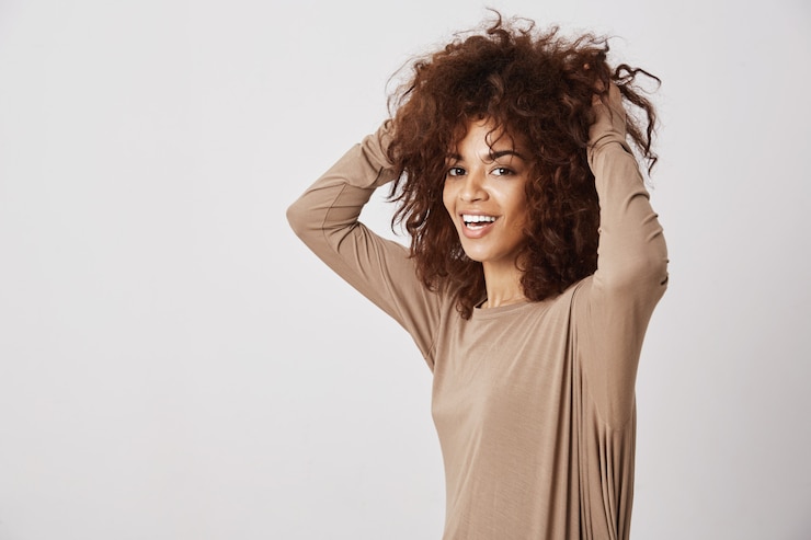 Foto grátis garota africana bonita feliz sorrindo tocando o cabelo dela. parede branca.