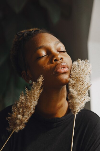 Garota africana em uma sala. Menina elegante com planta. Senhora com um suéter preto.