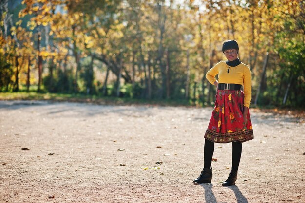 Garota afro-americana de vestido amarelo e vermelho no parque de outono dourado