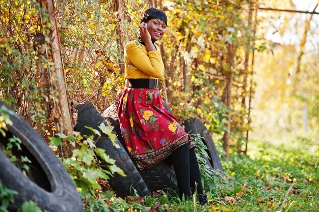 Garota afro-americana de vestido amarelo e vermelho no parque de outono dourado