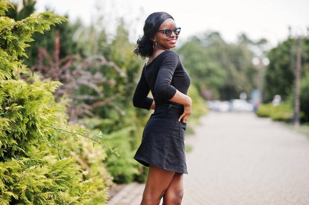 Garota afro-americana em óculos de sol, roupas pretas e camisa posou ao ar livre Mulher negra na moda