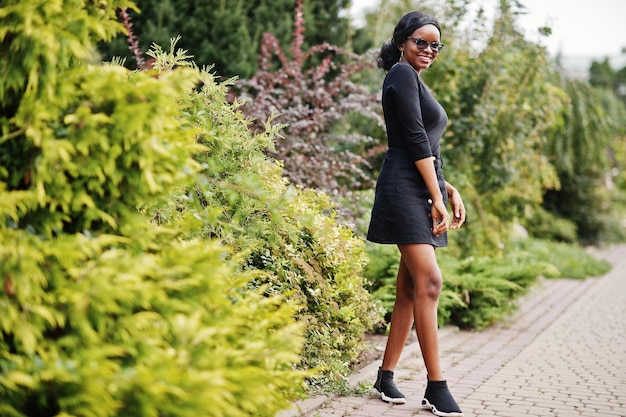 Garota afro-americana em óculos de sol, roupas pretas e camisa posou ao ar livre Mulher negra na moda