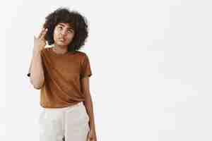 Foto grátis garota afro-americana sombria e insatisfeita com penteado encaracolado em uma camiseta marrom morrendo de tédio e aborrecimento revirando as pálpebras fazendo o dedo atirar na cabeça