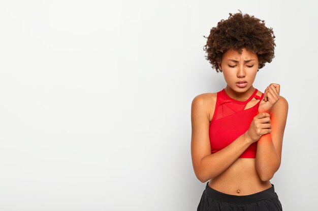 Garota afro descontente machucou o braço durante o treino, toca o pulso, sente dor, precisa ver um cirurgião, usa roupa casual