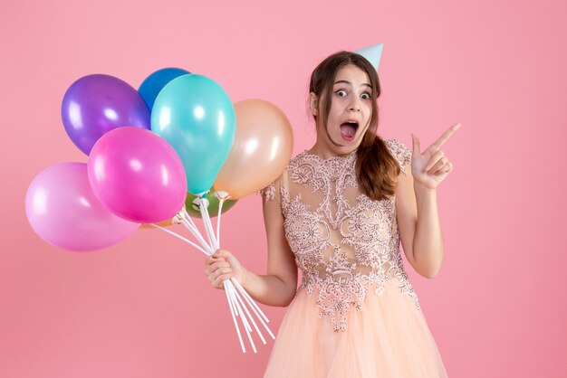 garota alegre com boné de festa segurando balões rosa