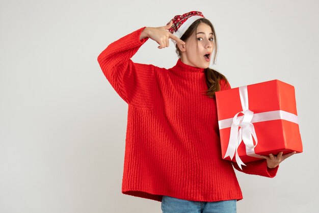 Garota animada com vista frontal e chapéu de Papai Noel apontando para o presente de Natal