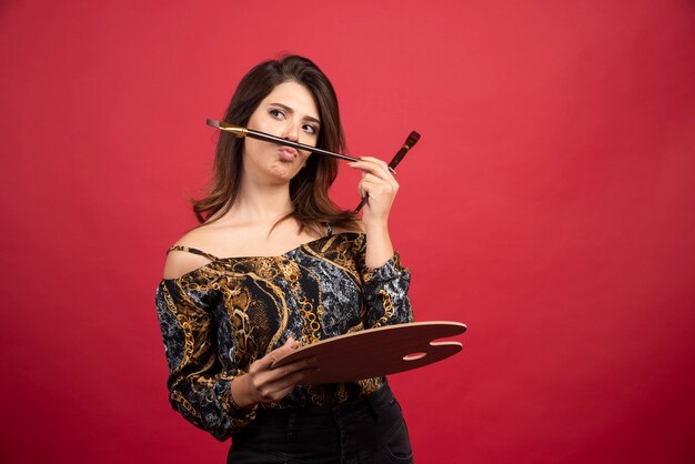 Garota artista posando com sua paleta de madeira e pincel.