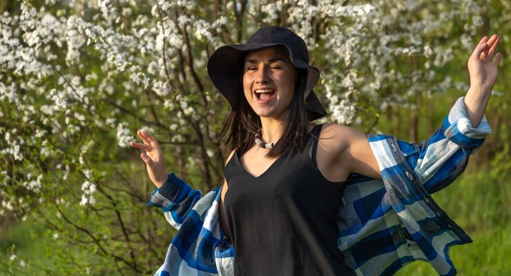 Foto grátis garota atraente com um chapéu entre as árvores floridas, na primavera, em um estilo casual.