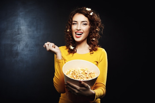 Garota atraente, comendo saborosa pipoca doce salgada, assistindo programas de tv