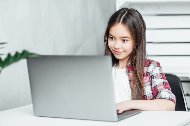 Garota atraente e inspirada de cabelos escuros de cabelos escuros enquanto está sentada à mesa do notebook em casa